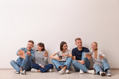 Photo of Group of people using different gadgets near white wall indoors. Modern technology