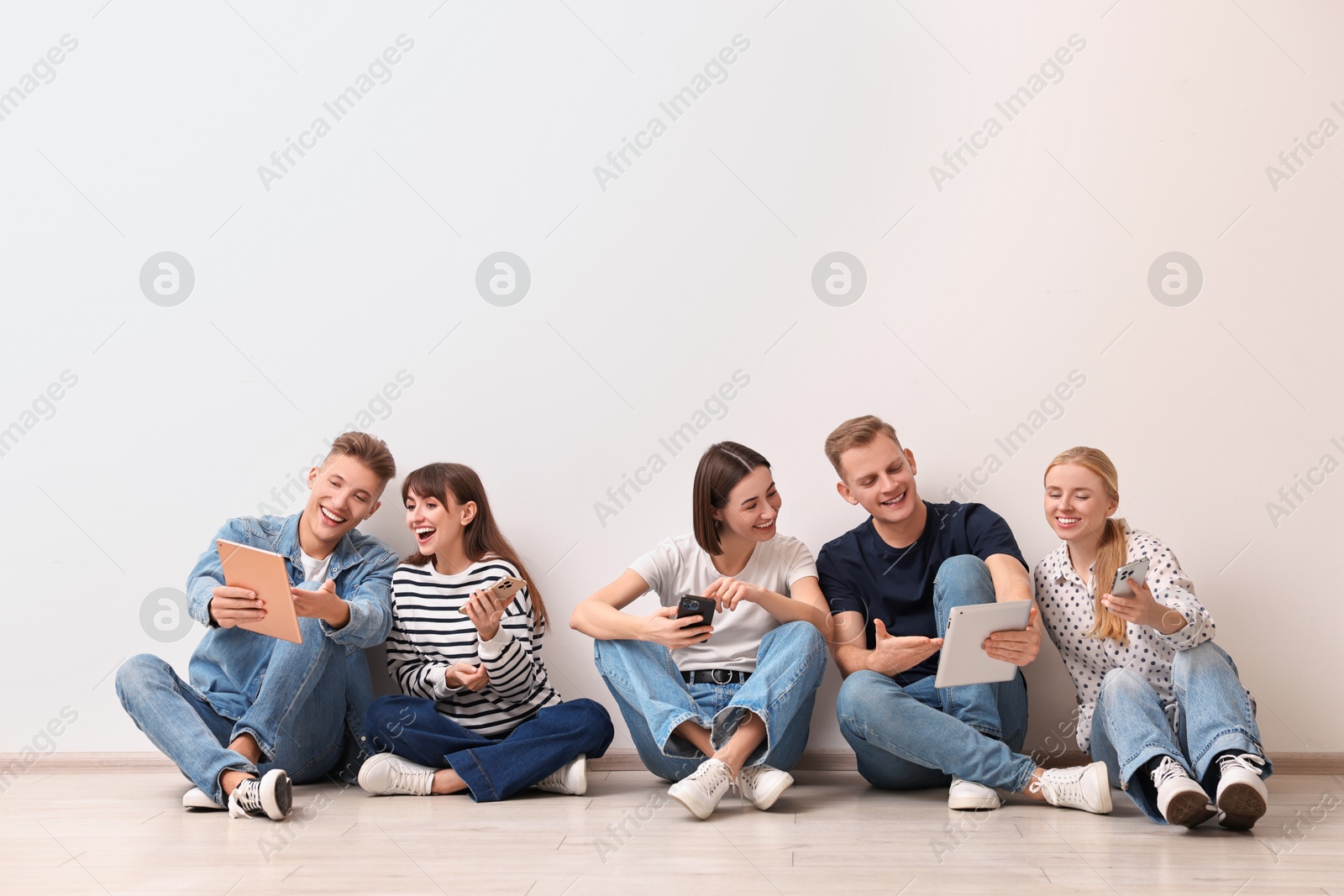 Photo of Group of people using different gadgets near white wall indoors. Modern technology