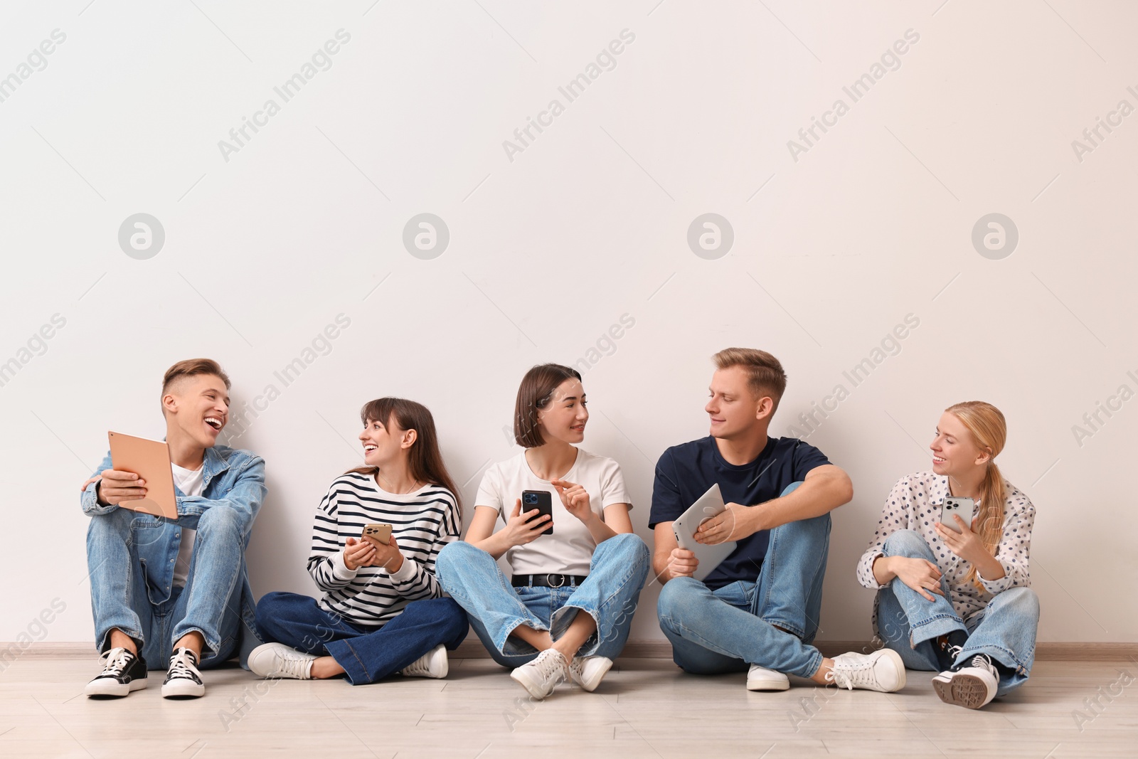 Photo of Group of people using different gadgets near white wall indoors. Modern technology