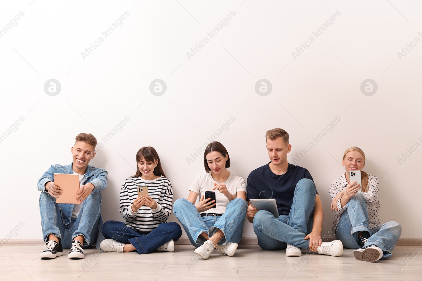 Photo of Group of people using different gadgets near white wall indoors. Modern technology