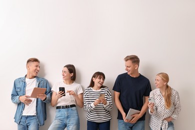 Photo of Group of people using different gadgets near white wall indoors. Modern technology