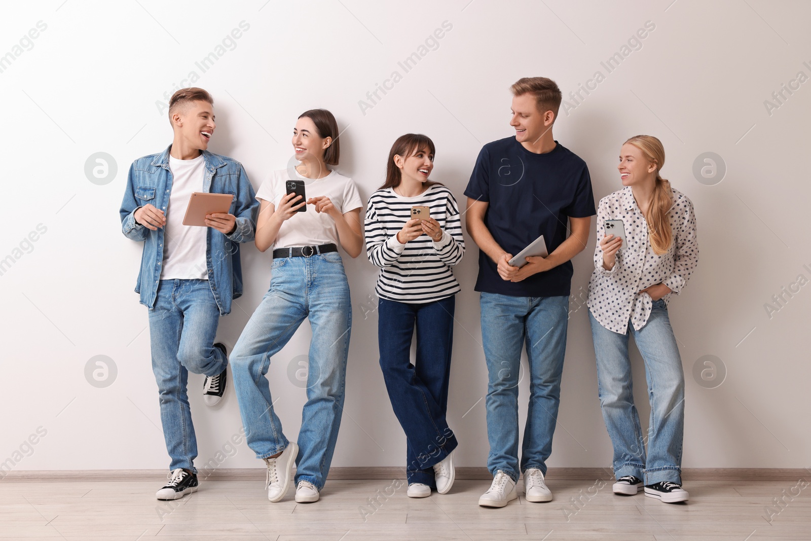 Photo of Group of people using different gadgets near white wall indoors. Modern technology