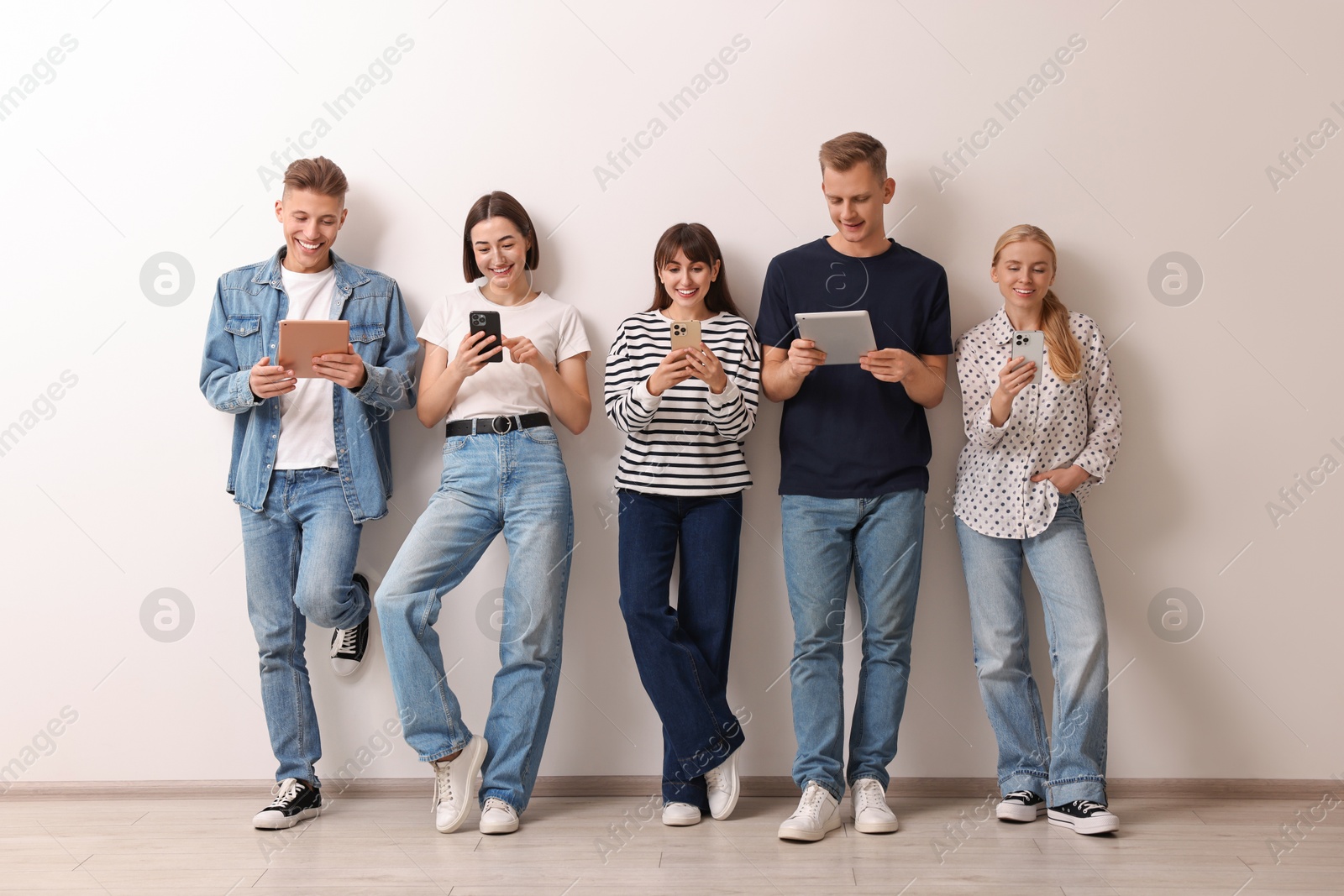 Photo of Group of people using different gadgets near white wall indoors. Modern technology