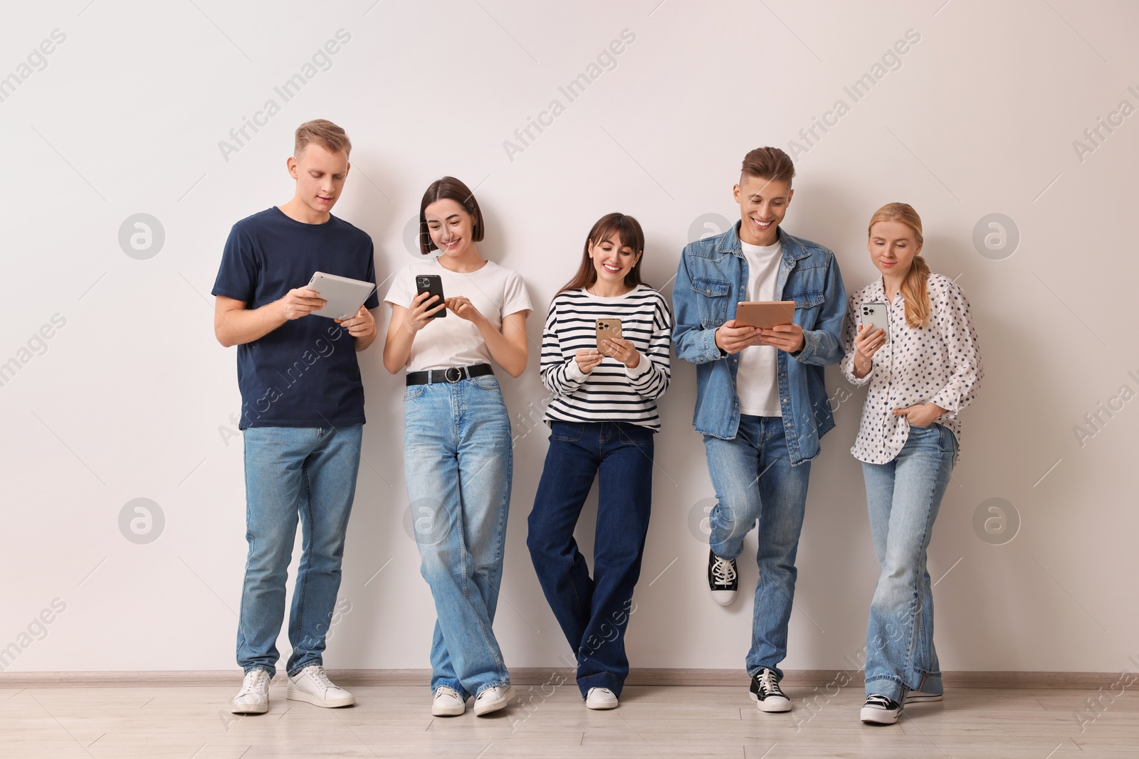 Photo of Group of people using different gadgets near white wall indoors. Modern technology