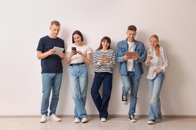 Photo of Group of people using different gadgets near white wall indoors. Modern technology