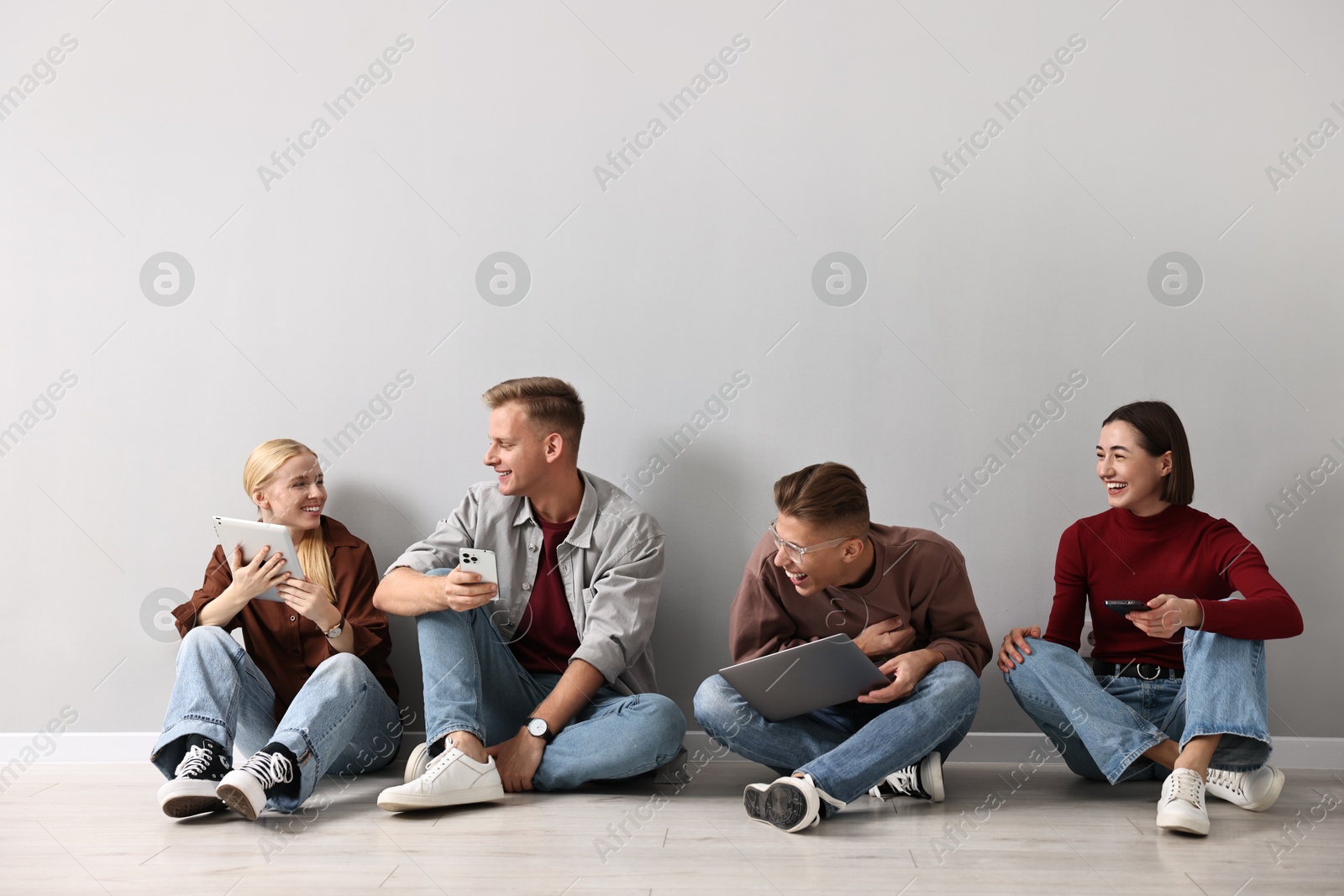 Photo of Group of people using different gadgets near light grey wall indoors. Modern technology