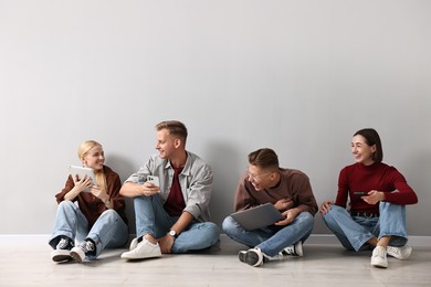 Photo of Group of people using different gadgets near light grey wall indoors. Modern technology