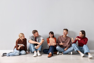 Photo of Group of people using different gadgets near light grey wall indoors. Modern technology