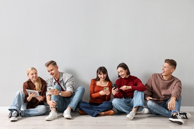 Photo of Group of people using different gadgets near light grey wall indoors. Modern technology