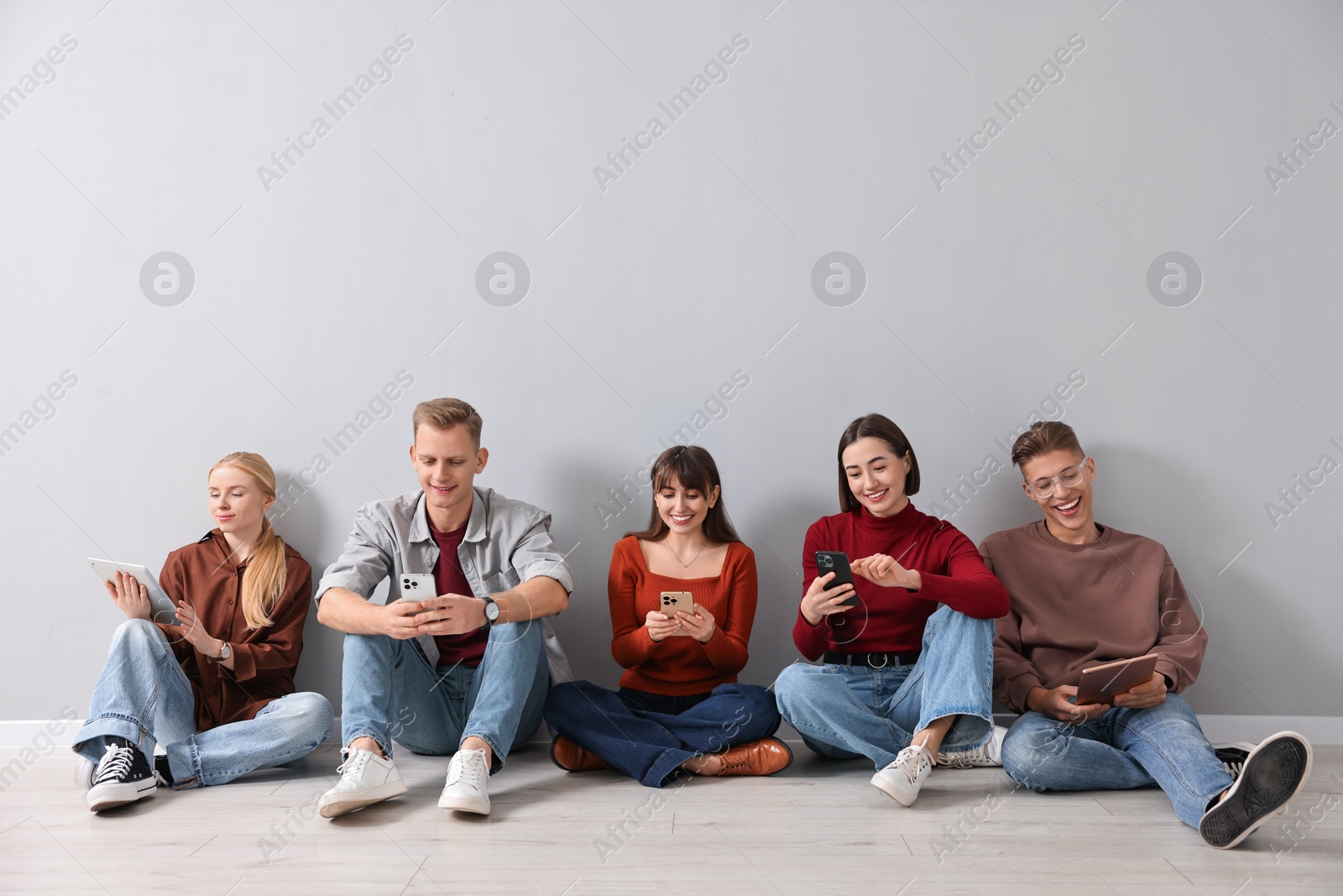 Photo of Group of people using different gadgets near light grey wall indoors. Modern technology