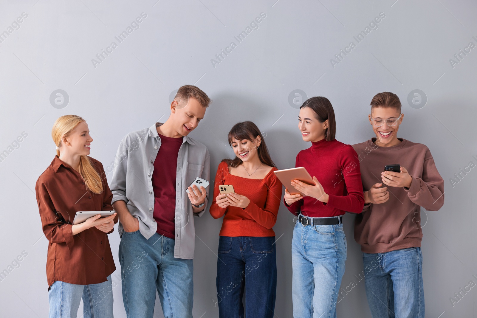 Photo of Group of people using different gadgets near light grey wall indoors. Modern technology