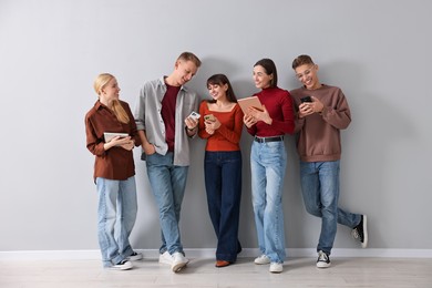 Photo of Group of people using different gadgets near light grey wall indoors. Modern technology