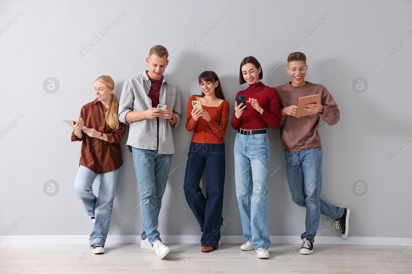 Photo of Group of people using different gadgets near light grey wall indoors. Modern technology