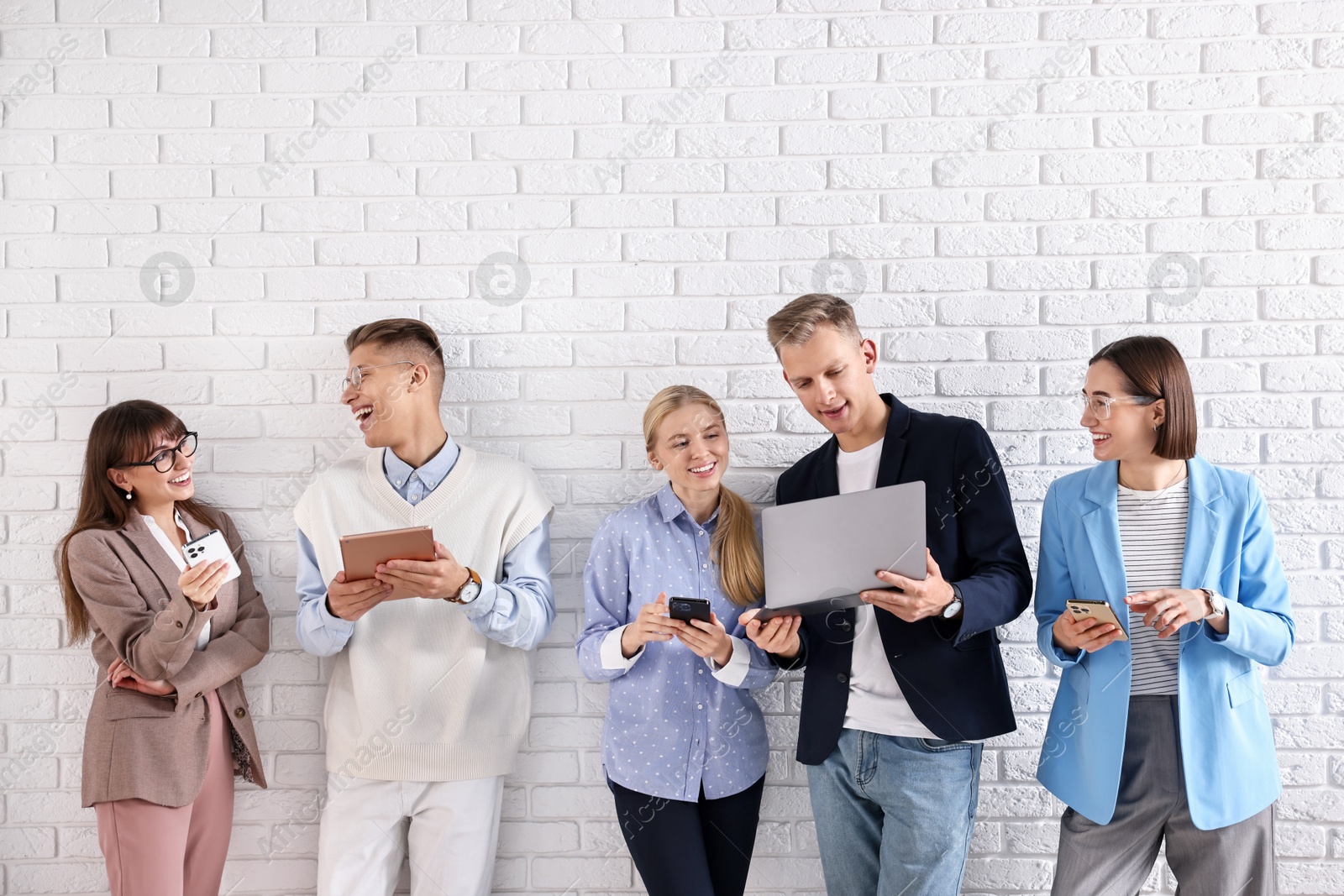 Photo of Group of people using different gadgets near white brick wall indoors. Modern technology