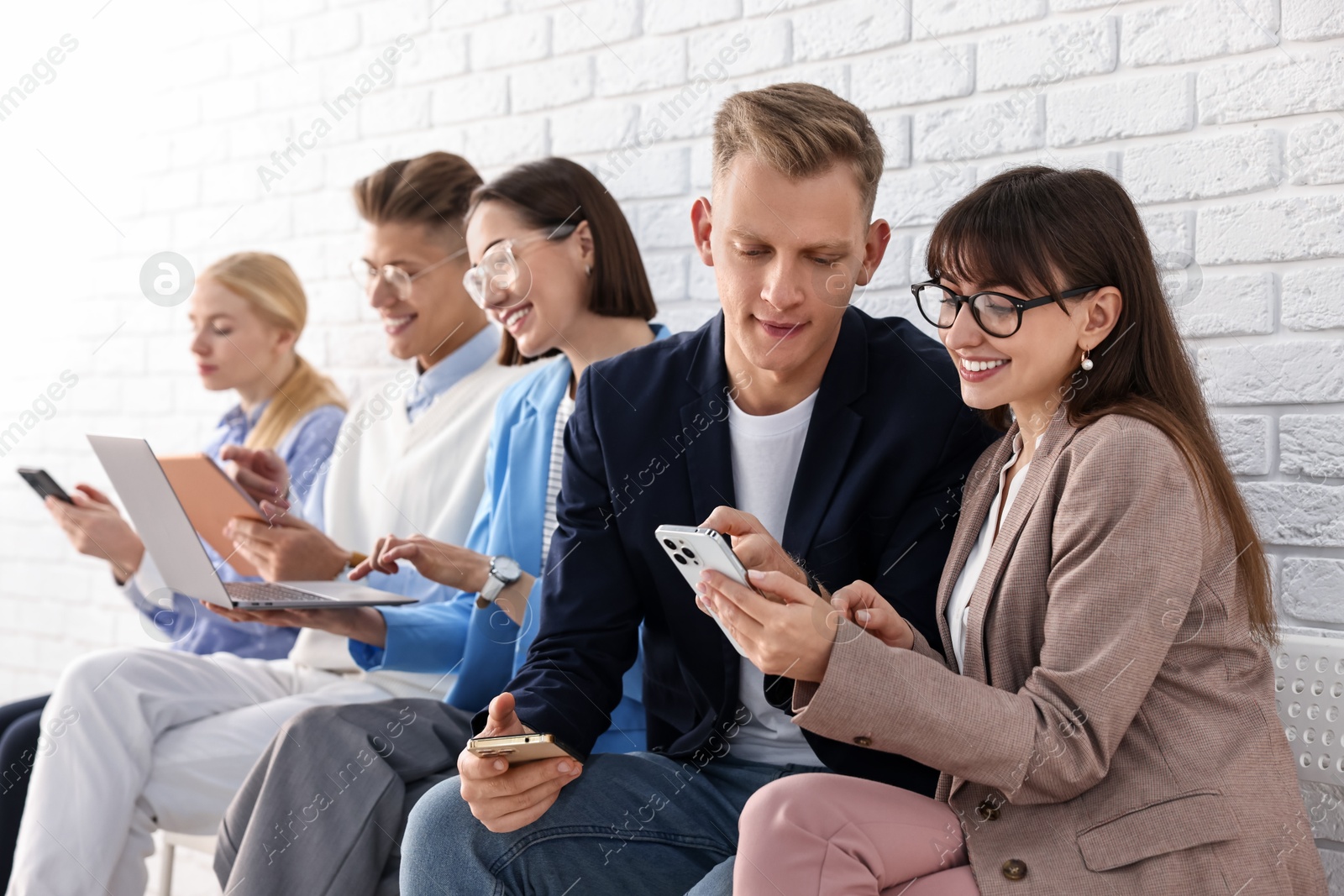 Photo of Group of people using different gadgets near white brick wall indoors. Modern technology