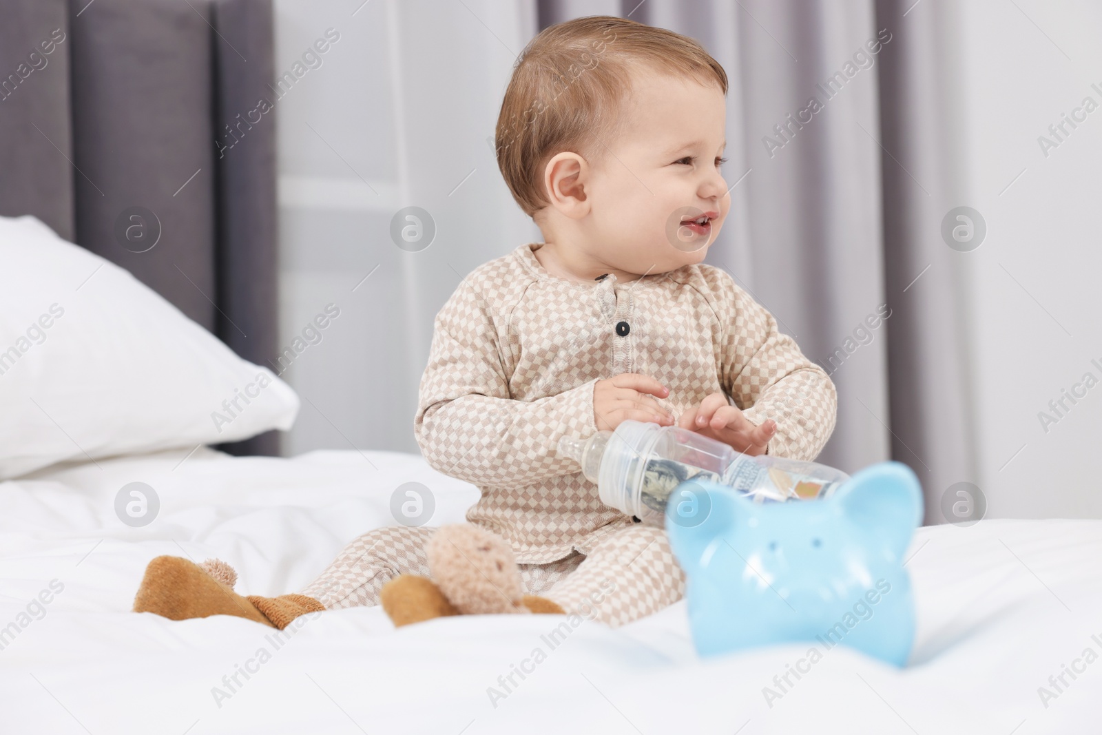 Photo of Cute little baby with money in bottle and piggybank on bed at home