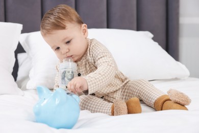 Photo of Cute little baby with money in bottle and piggybank on bed at home