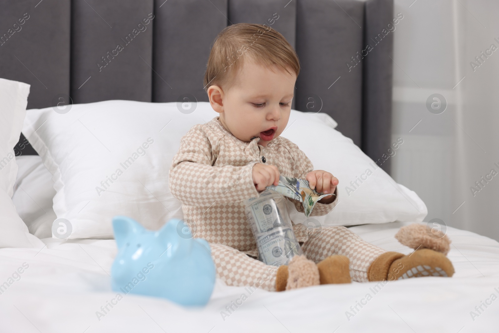 Photo of Cute little baby with money in bottle and piggybank on bed at home