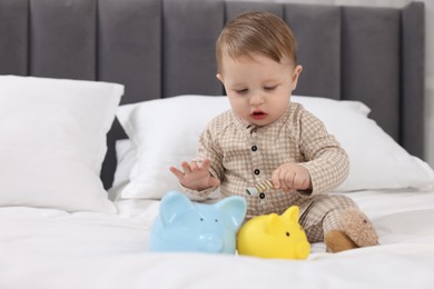 Photo of Cute little baby with piggybanks on bed at home