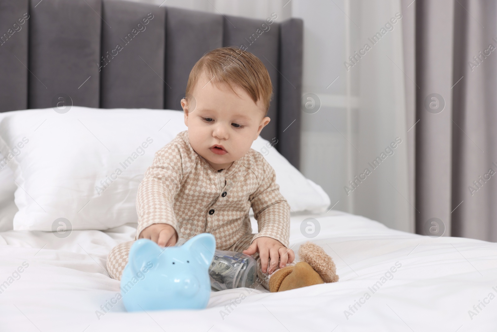 Photo of Cute little baby with piggybank on bed at home