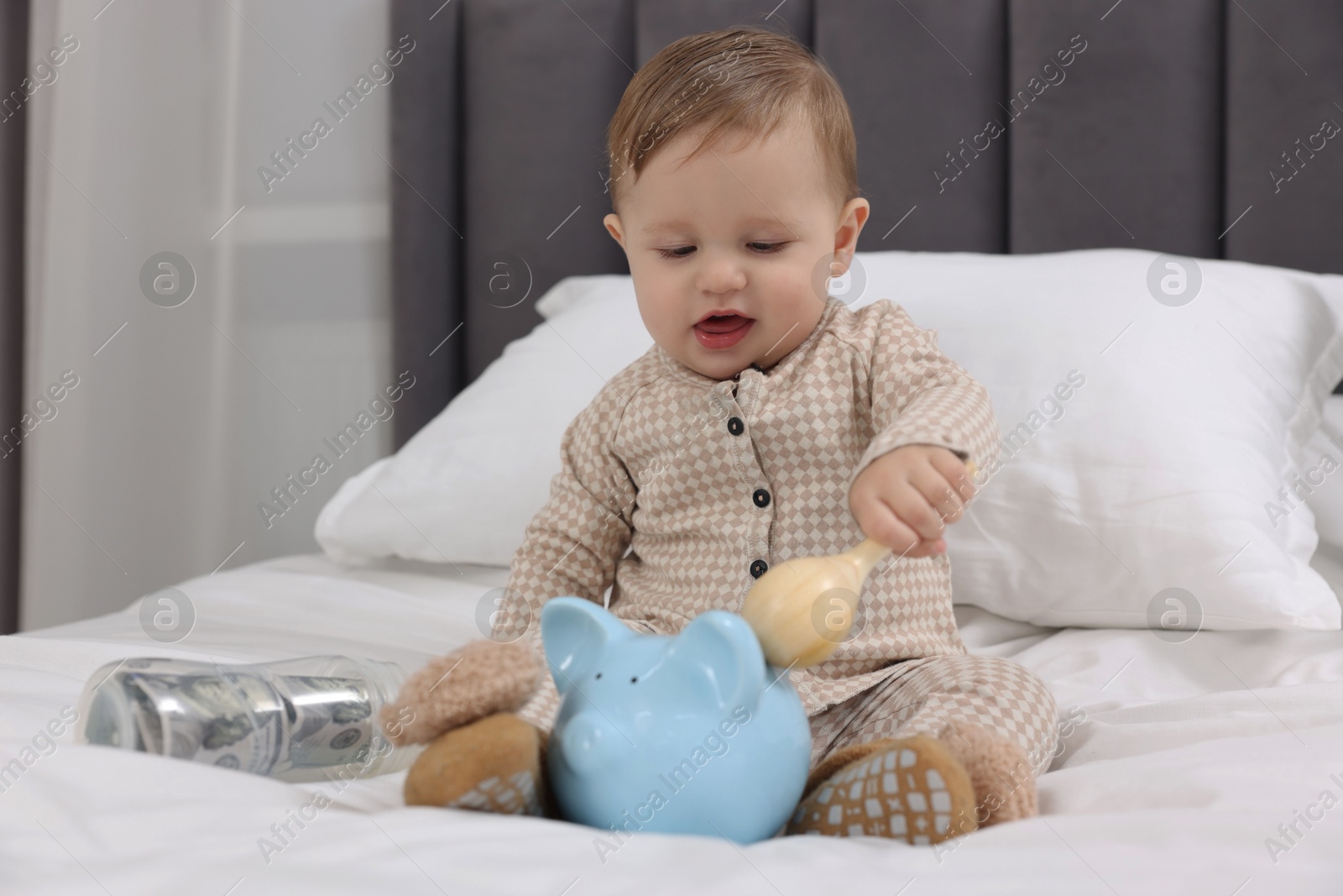 Photo of Cute little baby with money in bottle, toy and piggybank on bed at home