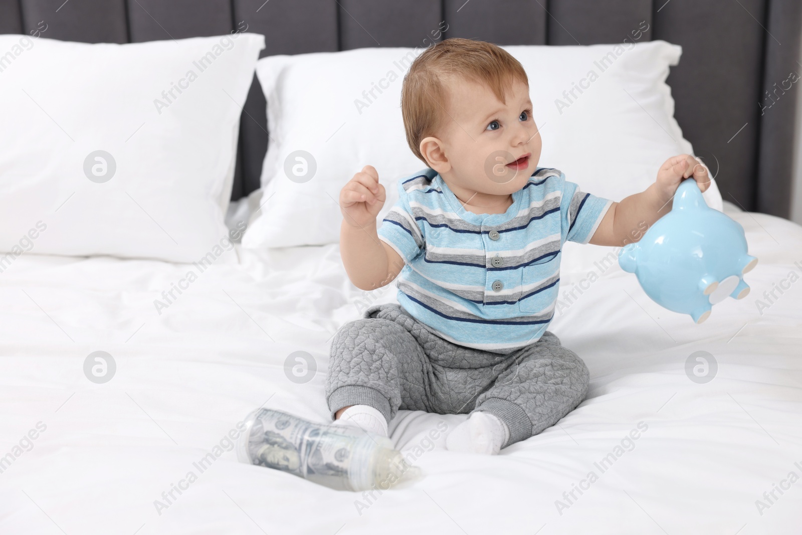 Photo of Cute little baby with money in bottle and piggybank on bed at home