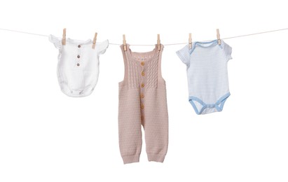 Different baby clothes drying on laundry line against white background