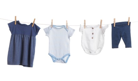 Different baby clothes drying on laundry line against white background