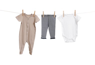 Different baby clothes drying on laundry line against white background