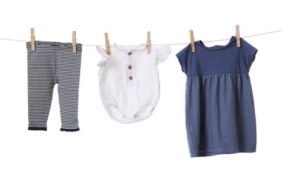 Photo of Different baby clothes drying on laundry line against white background