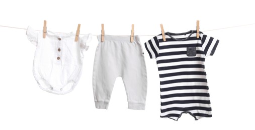 Different baby clothes drying on laundry line against white background