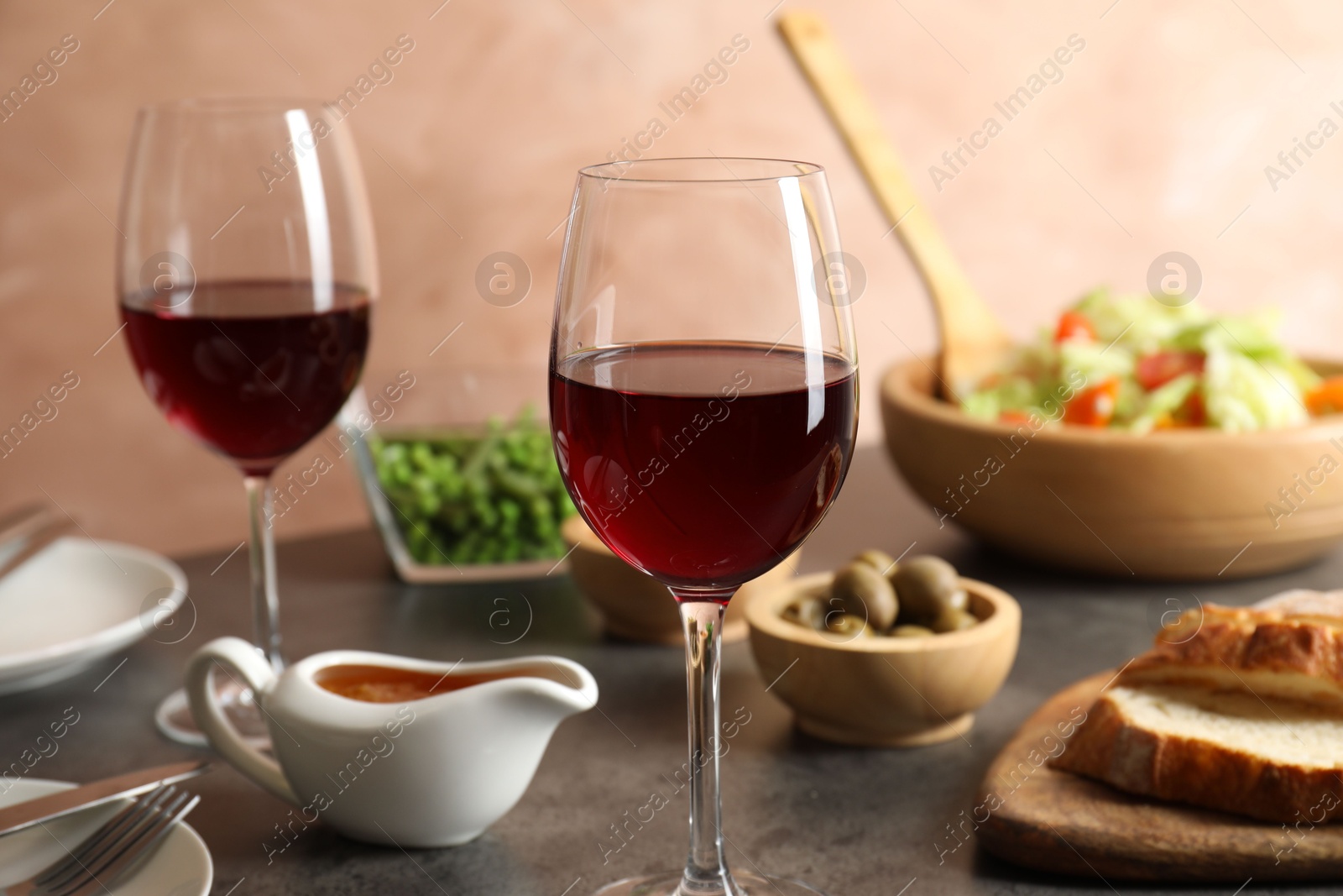 Photo of Red wine and delicious dinner served on grey table, closeup