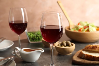 Photo of Red wine and delicious dinner served on grey table, closeup