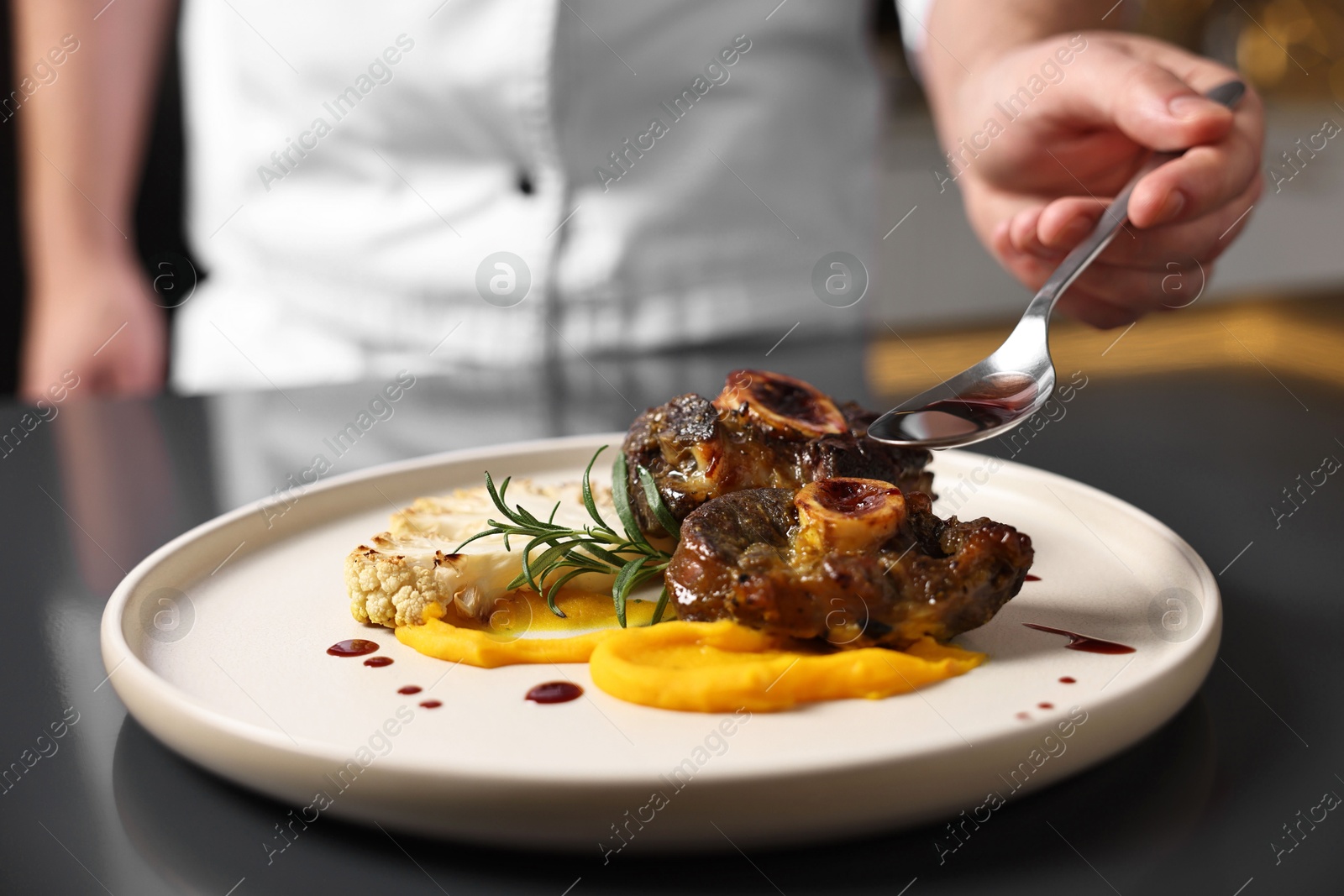 Photo of Professional chef adding sauce to delicious dish at table indoors, closeup