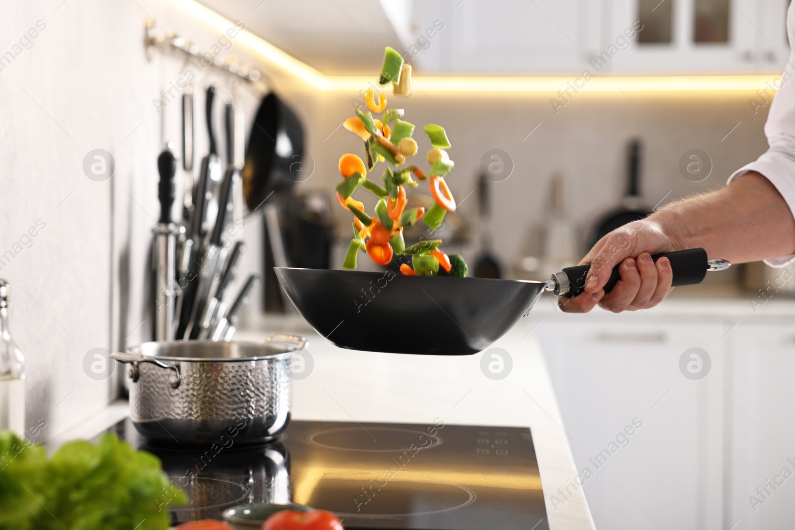 Photo of Professional chef mixing vegetables in wok at kitchen, closeup