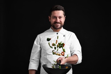 Photo of Professional chef mixing vegetables in wok on black background