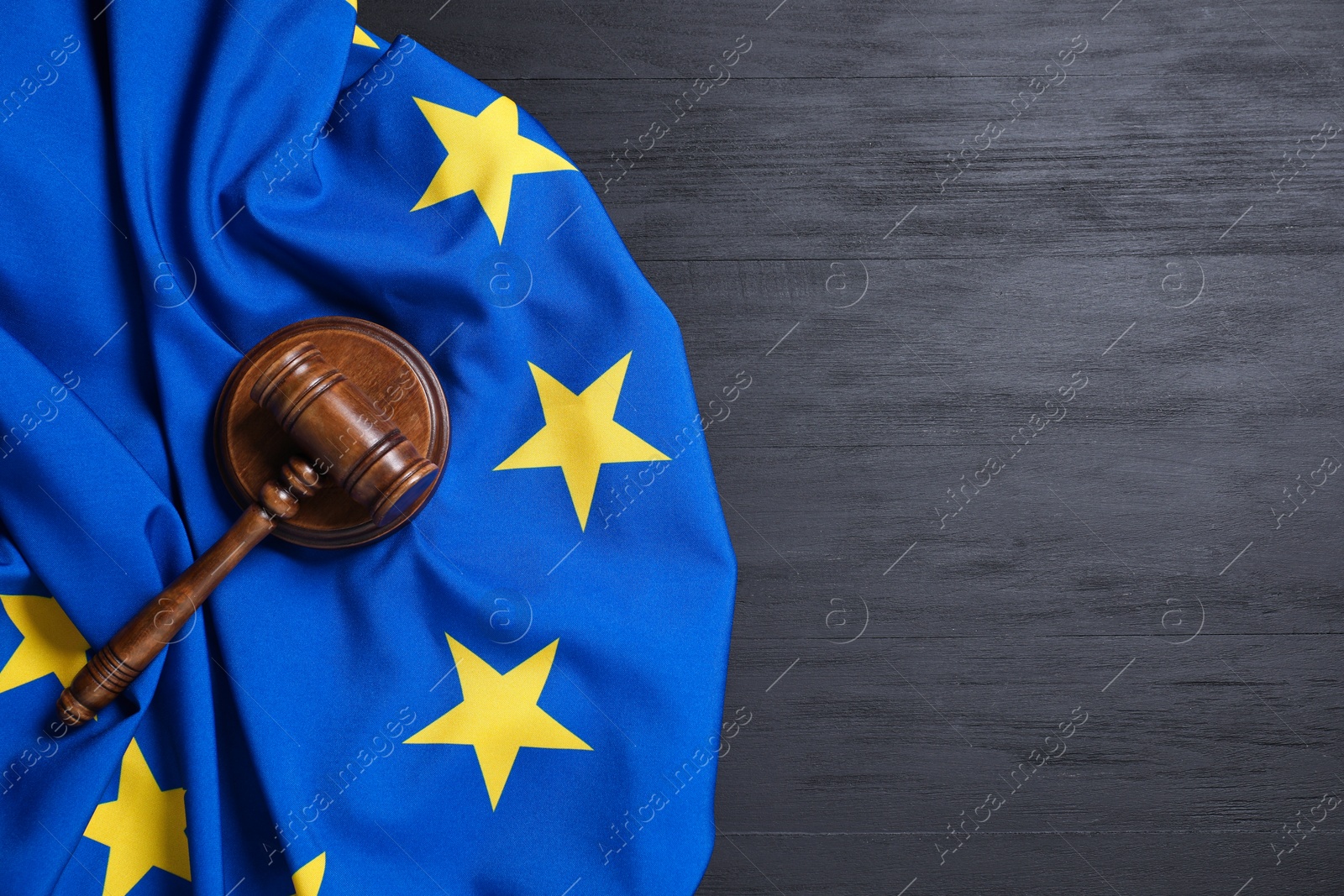 Photo of Judge's gavel and flag of European Union on grey wooden table, top view. Space for text