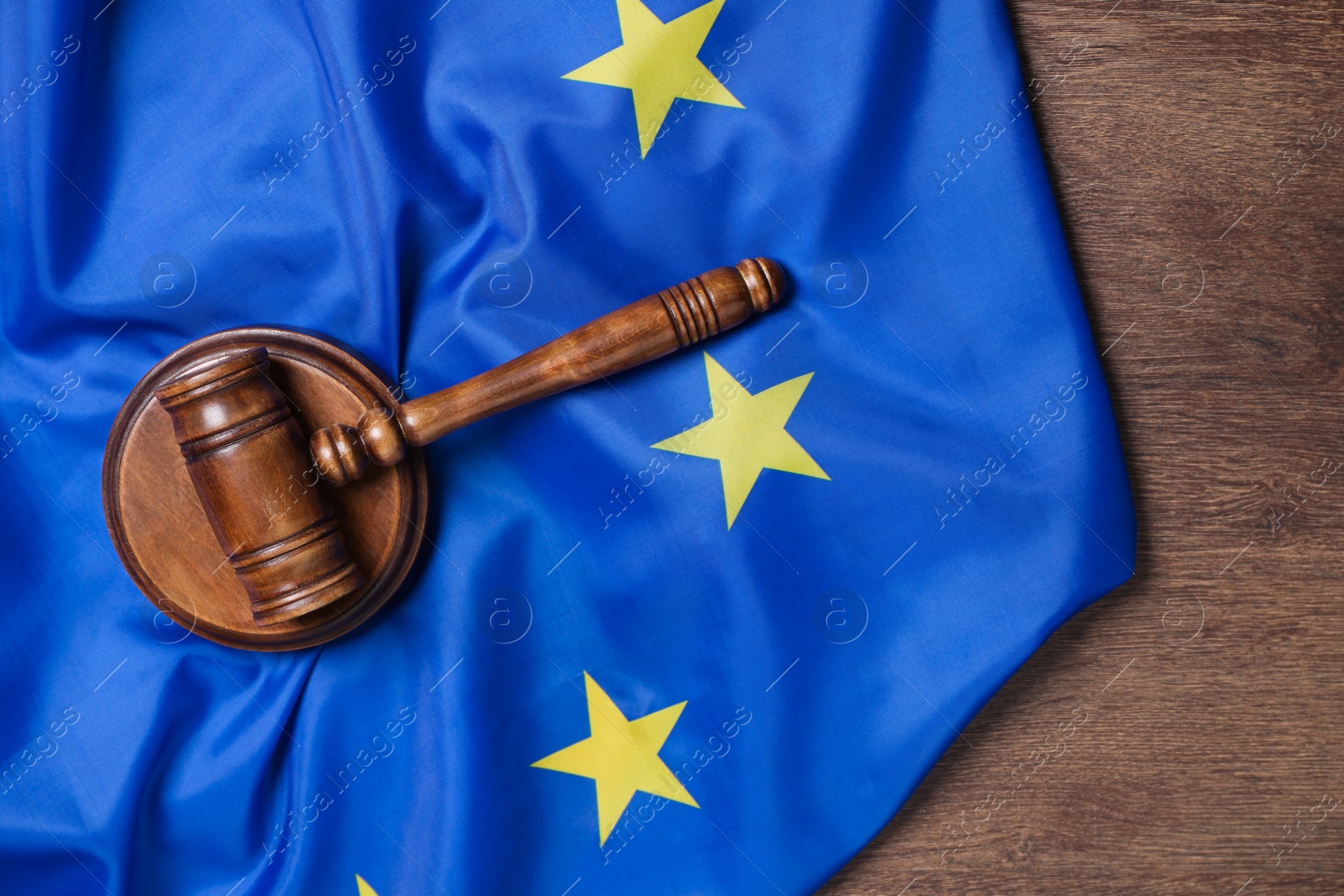 Photo of Judge's gavel and flag of European Union on wooden table, top view