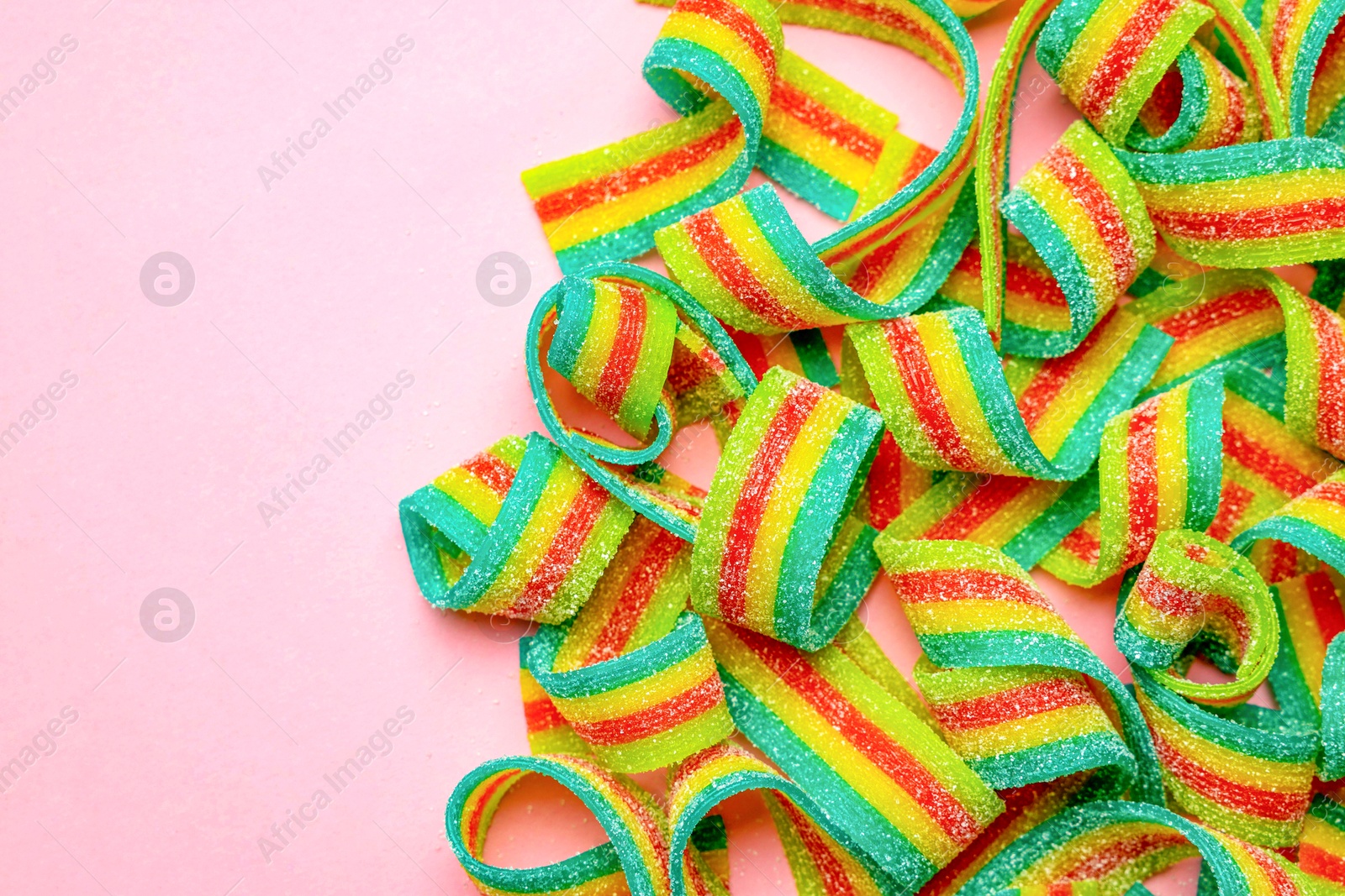 Photo of Tasty rainbow sour belts on pink background, top view. Space for text