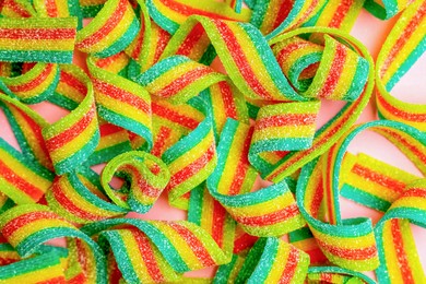 Photo of Tasty rainbow sour belts on pink background, top view