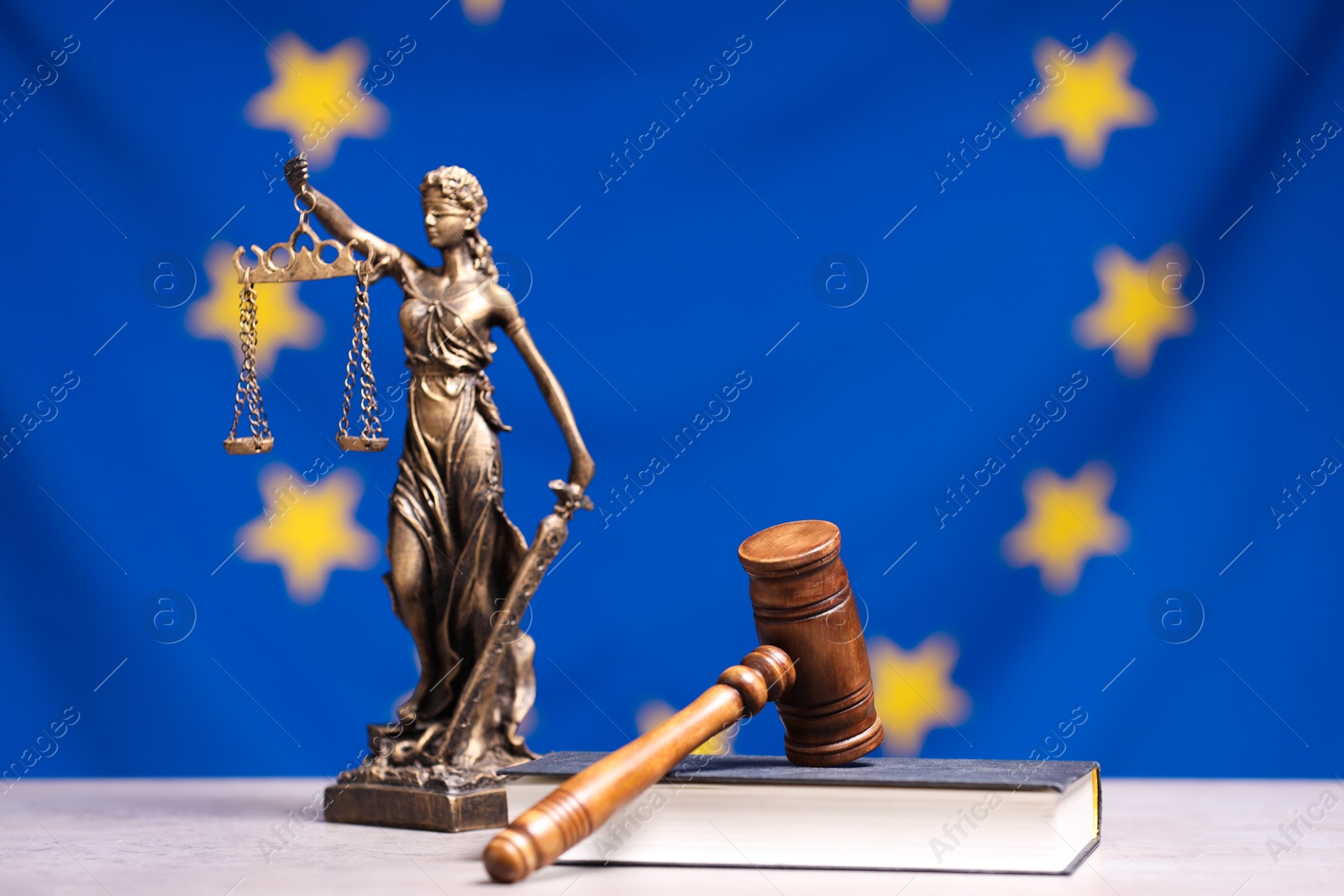 Photo of Judge's gavel, book and figure of Lady Justice on table against European Union flag