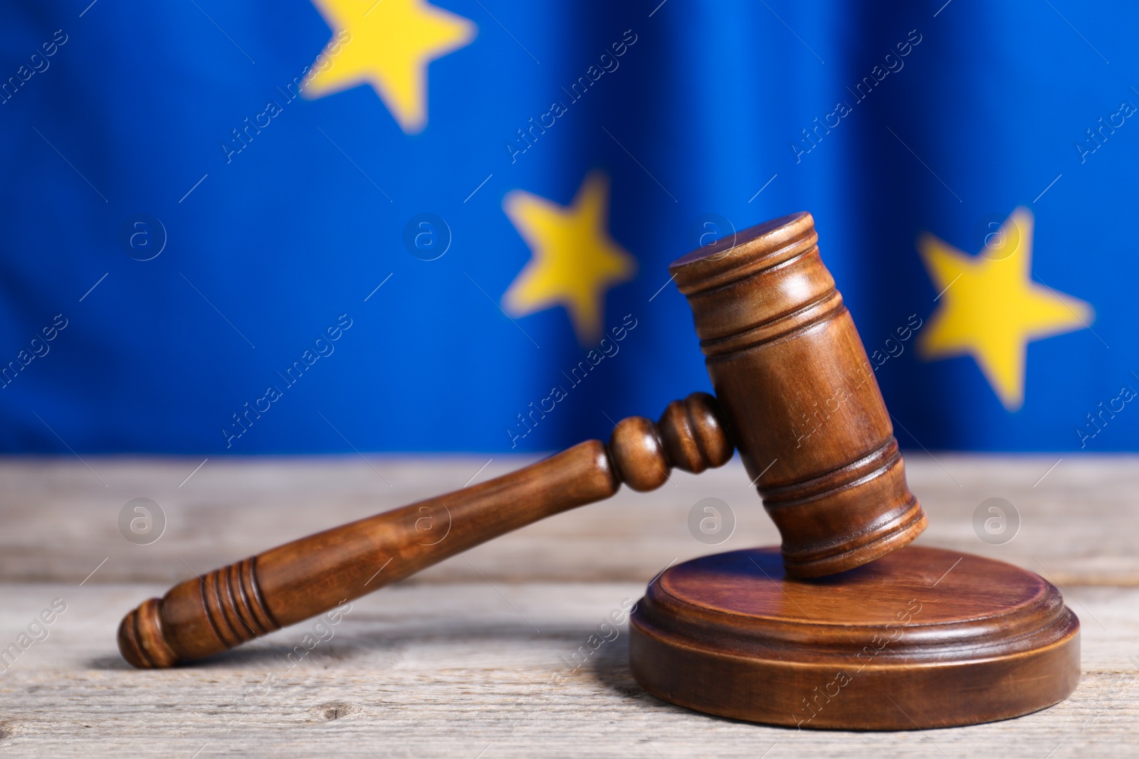 Photo of Judge's gavel on wooden table against European Union flag, closeup