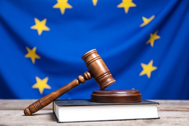 Photo of Judge's gavel on wooden table against European Union flag, closeup