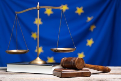 Photo of Judge's gavel, scales of justice and book on wooden table against European Union flag