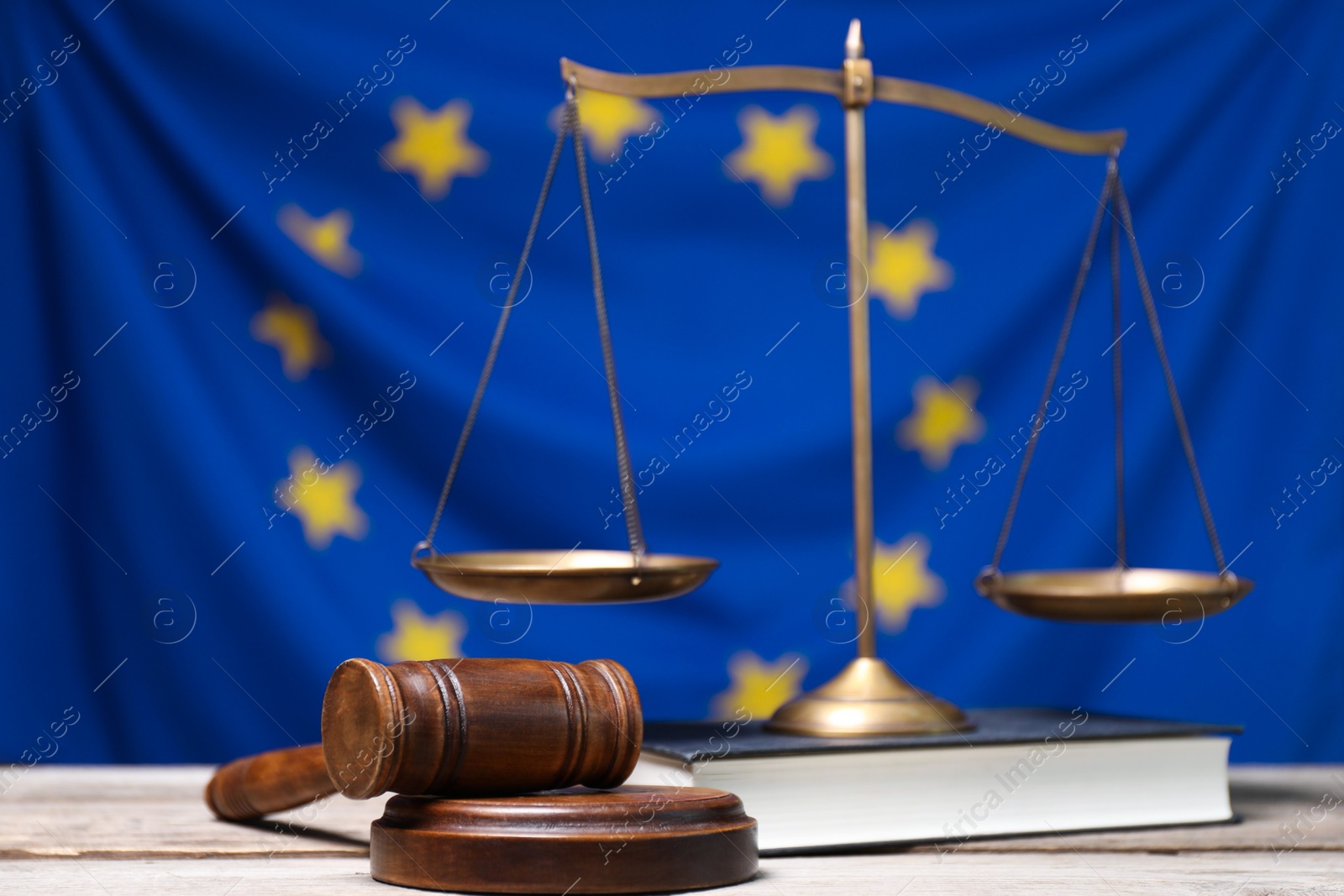 Photo of Judge's gavel, scales of justice and book on wooden table against European Union flag