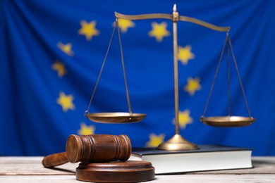 Photo of Judge's gavel, scales of justice and book on wooden table against European Union flag