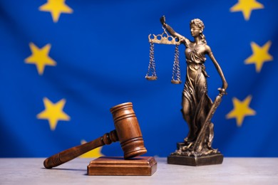 Photo of Figure of Lady Justice and judge's gavel on table against European Union flag