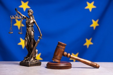 Photo of Figure of Lady Justice and judge's gavel on table against European Union flag