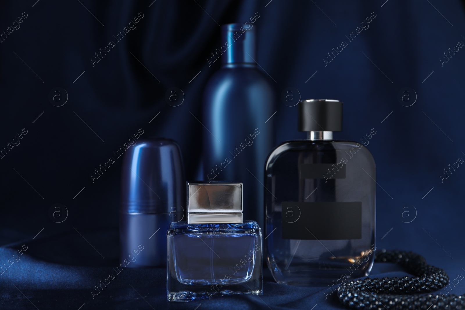 Photo of Bottles of perfumes, deodorant, shampoo and dark blue silk fabric