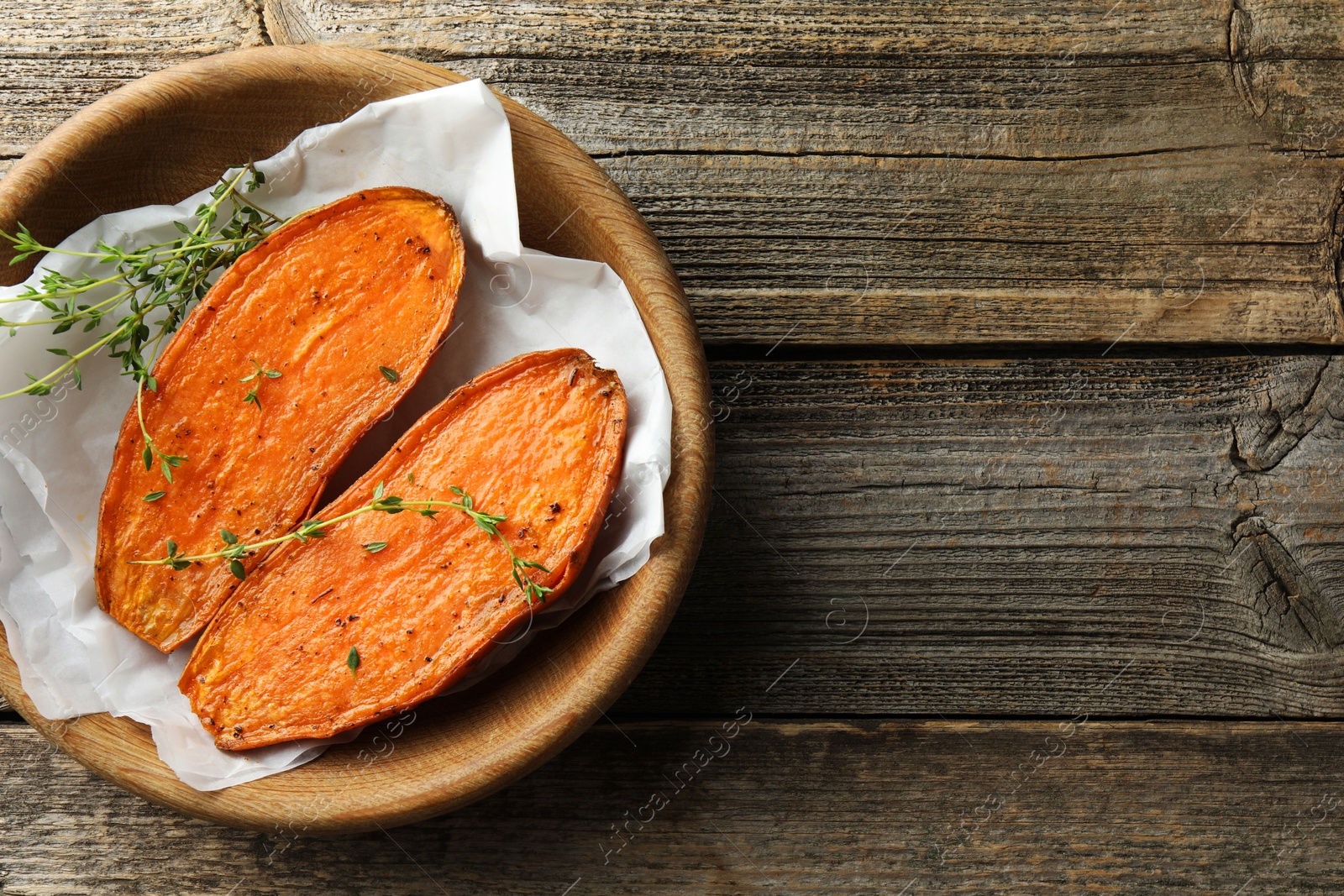 Photo of Halves of tasty cooked sweet potato with thyme on wooden table, top view. Space for text